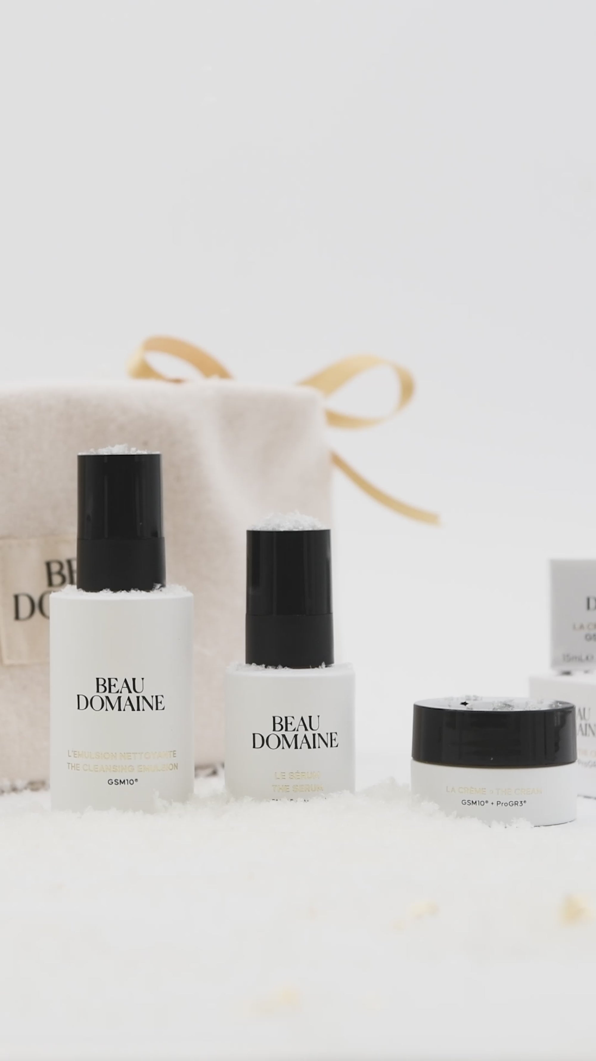Short video showing an animation of La Routine Découverte in the world of holiday celebrations, with the products lined up in front of the pouch against a clean white background and fake snow, and a hand taking the cream and removing it from view, presumably to use it